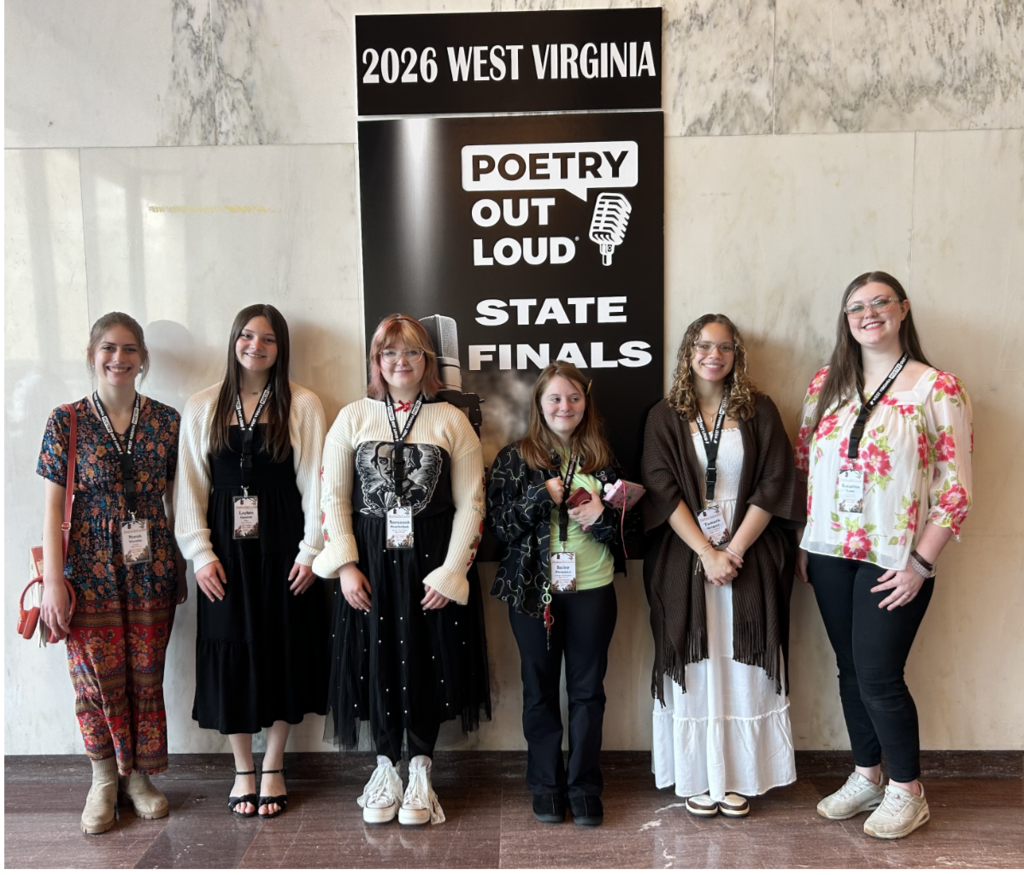 The six KCS students who reached the semifinal round of the WV Poetry Out Loud Competition posing for a picture against a wall. They are standing in front of a Poetry Out Loud State Finals poster.