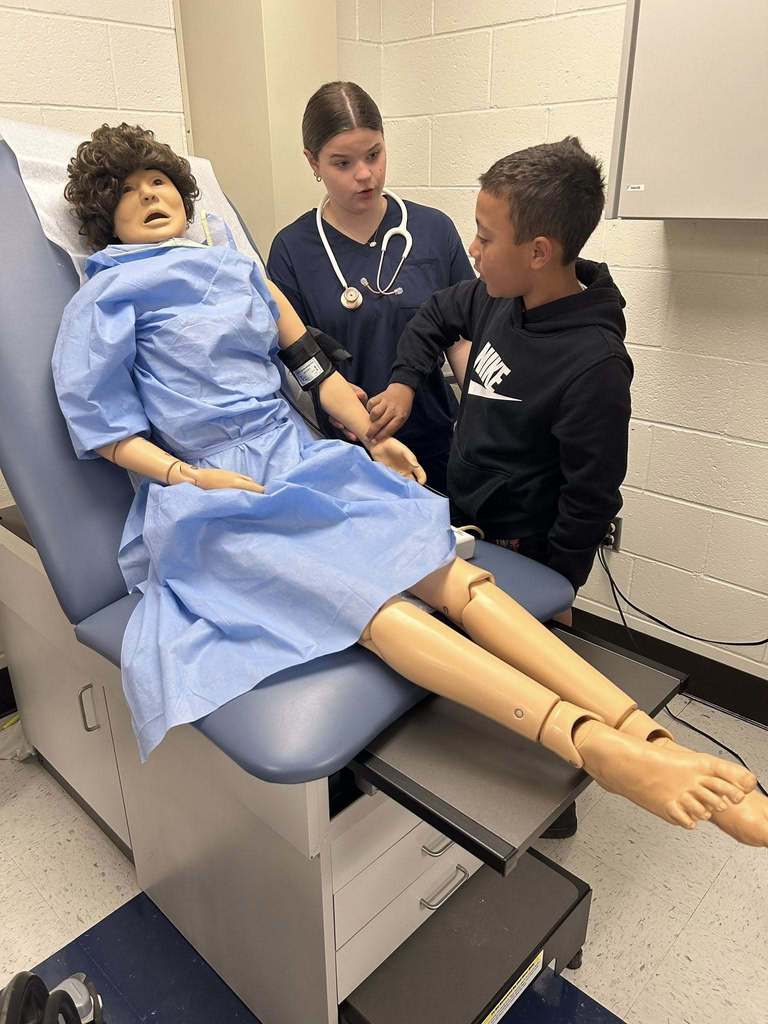 A ben franklin student watches and a nitro student check the pulse on a medical mannequin. 