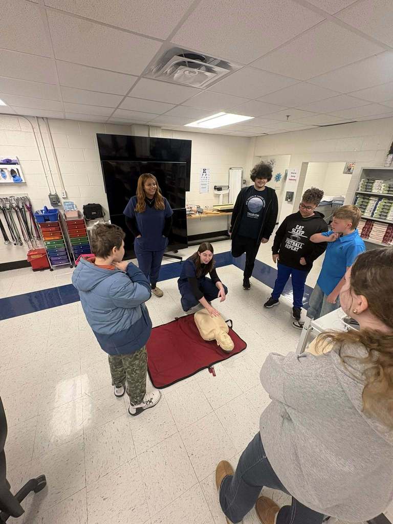 A ben franklin student is demonstrating how to do CPR on a medical mannequin as several nitro students are standing around her watching.