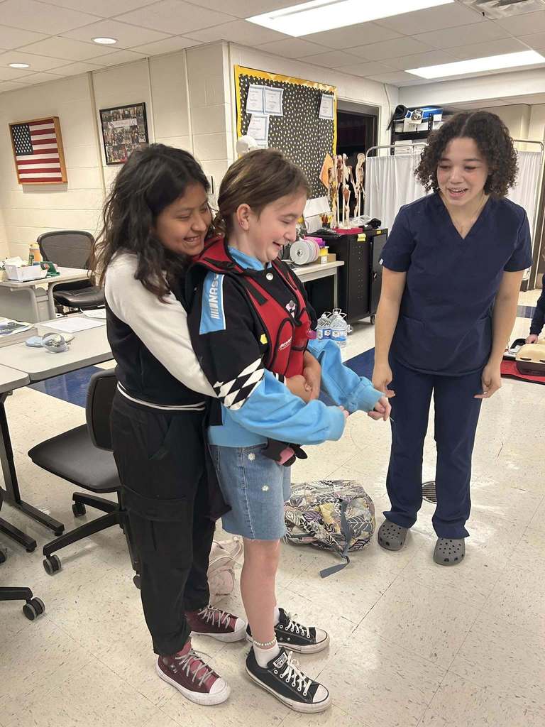 A nitro student is doing the Heimlich on one of her classmates during a lesson. A ben franklin student is providing feedback on the students technique.
