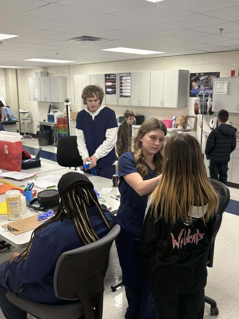 a ben franklin student is checking something on a nitro student. The nitro student's back is turned to the camera, so it is not clear what is being checked. 
