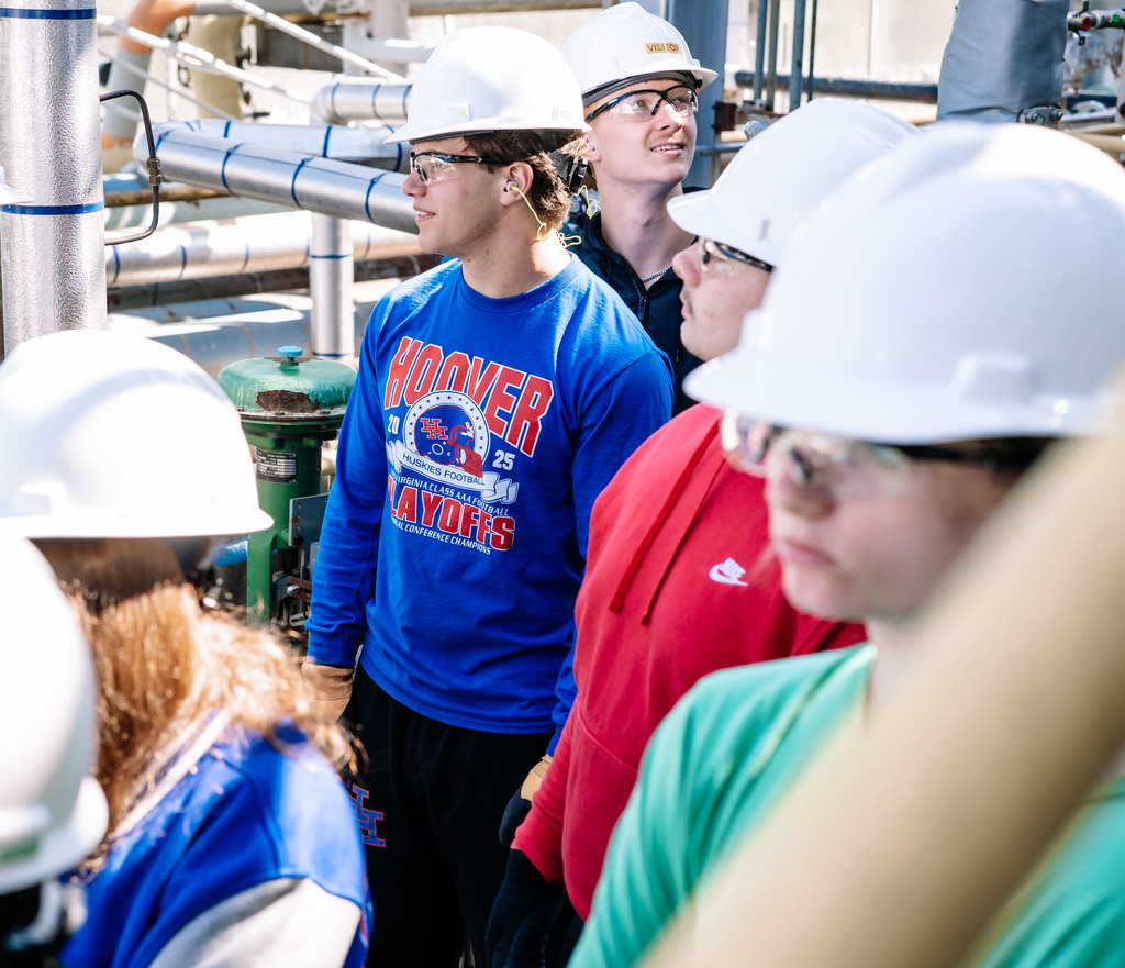 Students listen in on the tour of the DOW Plant, and are wearing a hard hat, safety glasses, safety gloves, and ear plugs. 
