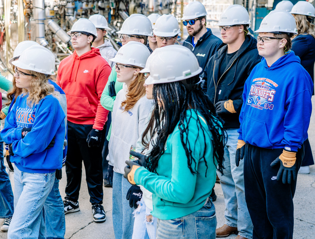 Students wearing hard hats, safety glasses, and safety gloves, are listening while a DOW Operator, not pictured, talks about DOW Operations.