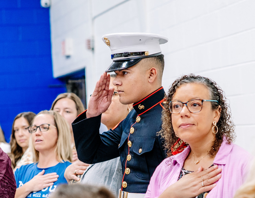 A Marine, in his dress blues, is saluting during the singing of the National Anthem. 