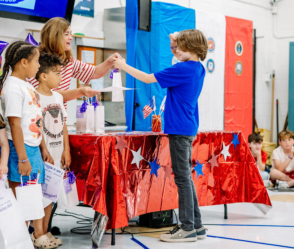 A Weberwood student with a family member in the military is getting his gift from a teacher. The student is saluting his teacher as she hands him the small white bag.