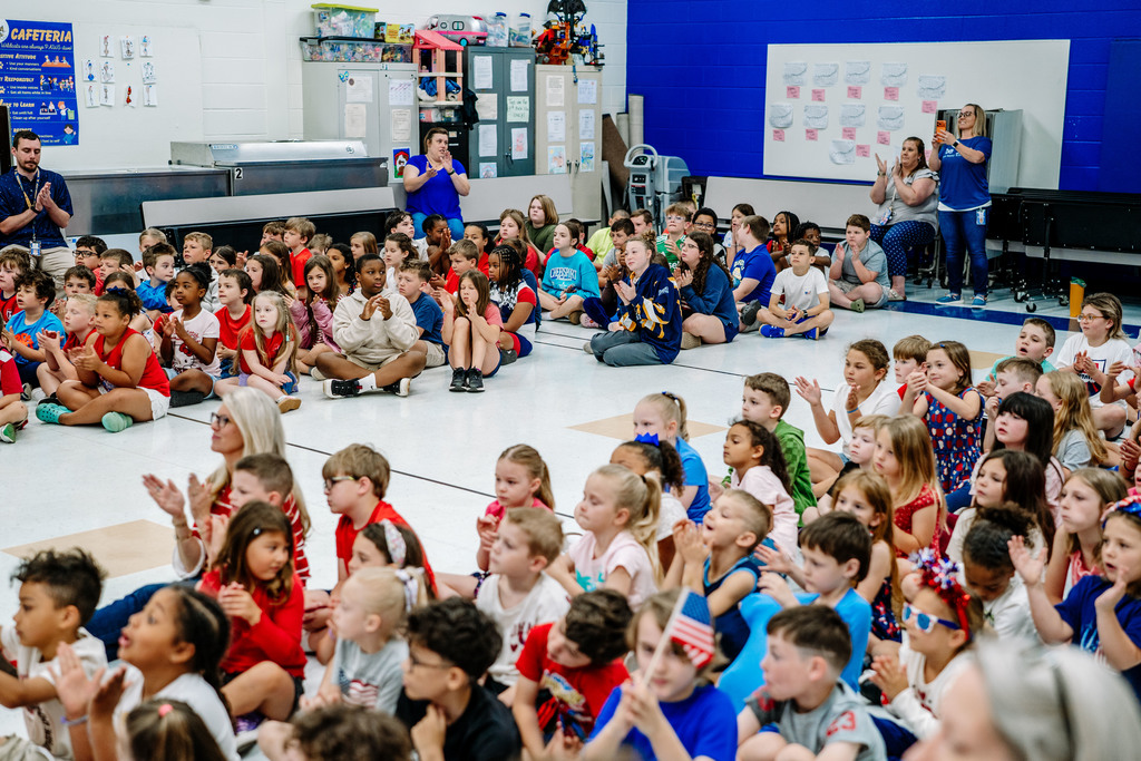 The student body at Weberwood Elementary is sitting on the floor of the cafeteria and applauding. 