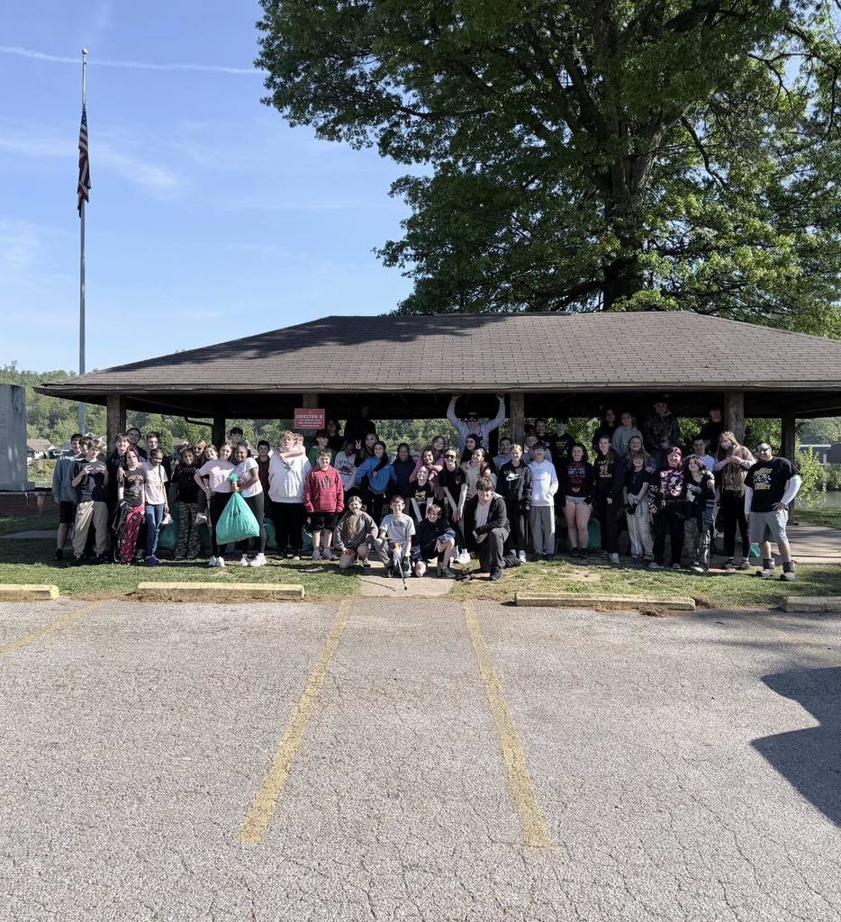 A group picture of students standing under a picnic shelter in a park. 