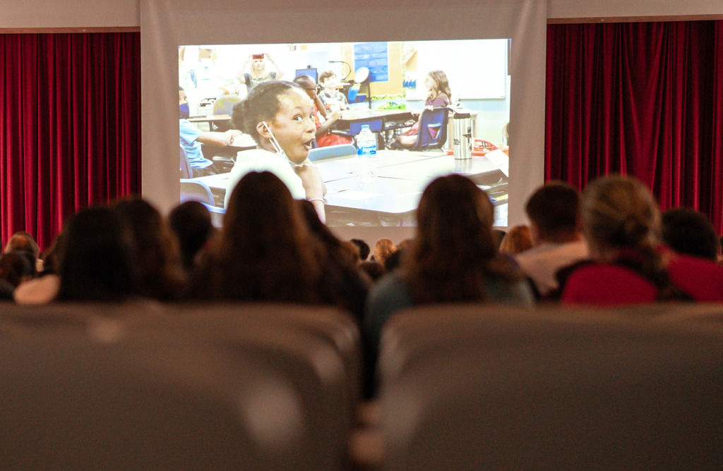 A projector screen showing a video about Sharon's non-profit, Space Kids Global. A student in the video is making an excited face. 