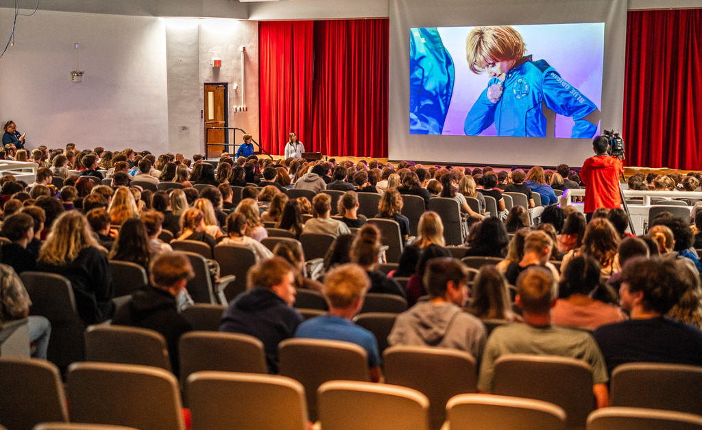 Students watching a video of Sharon getting ready for her space flight on a large projection screen in the school's auditorium. 
