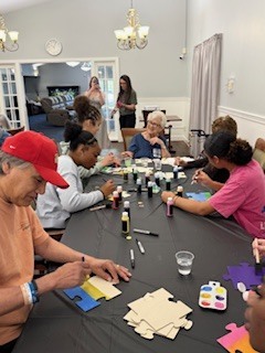 A group of students and nursing home residents are sitting around a table doing a painting project.