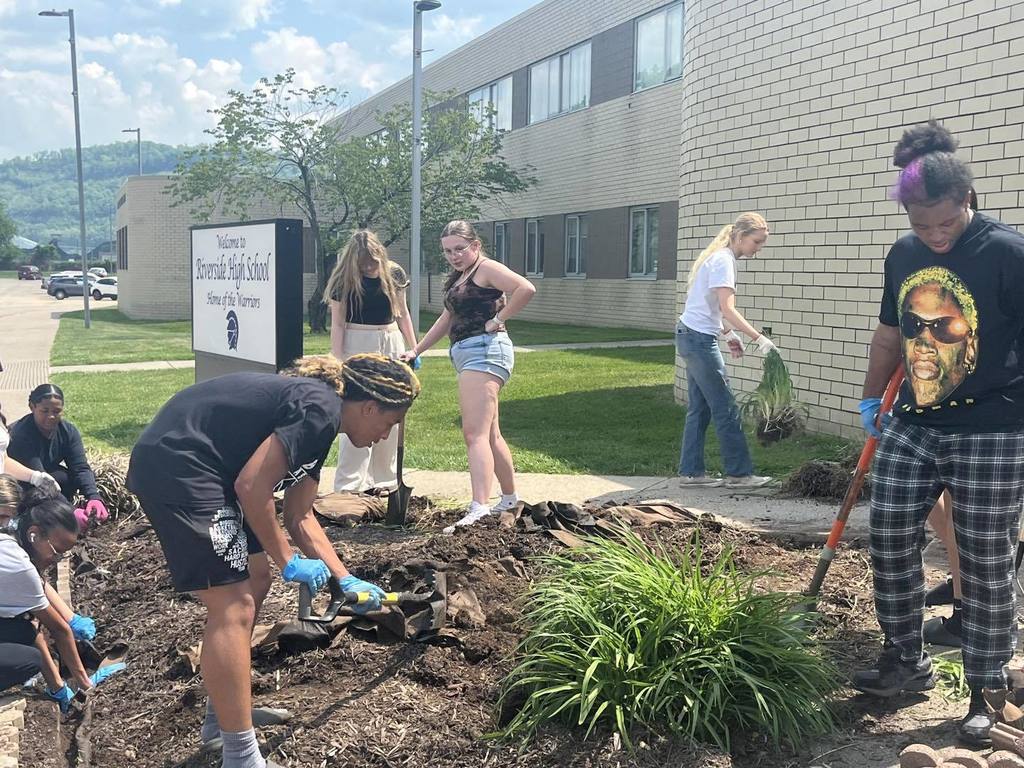 Students working in the flower bed in front of their school. Students are using shovels and other garden tools to get the area ready for new flowers to be planted. 