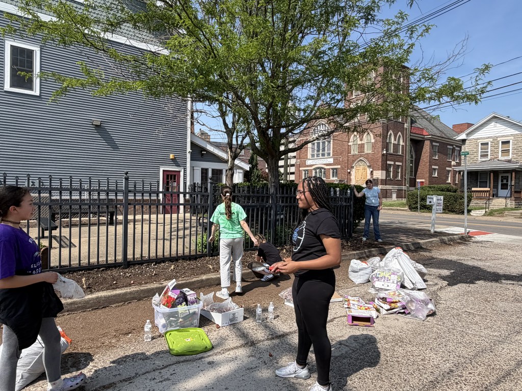 Two students are standing up talking to each other while doing a community service project. Behind them other students are digging in the dirt.