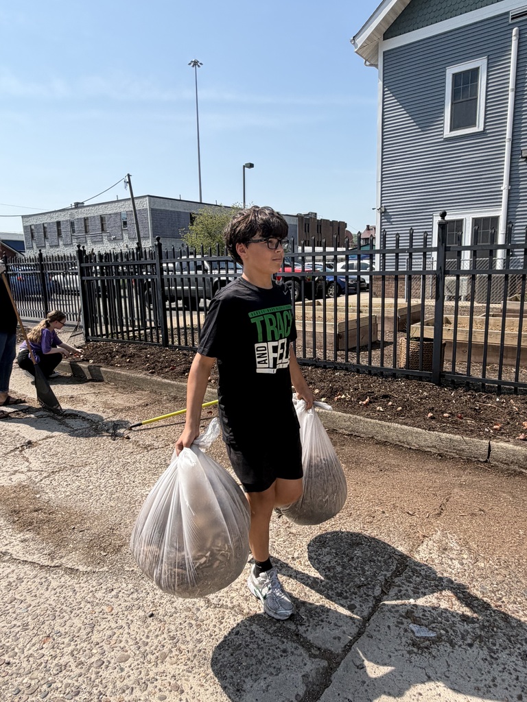 A student carrying two clear trash bags that are full of leaves and other debris. 