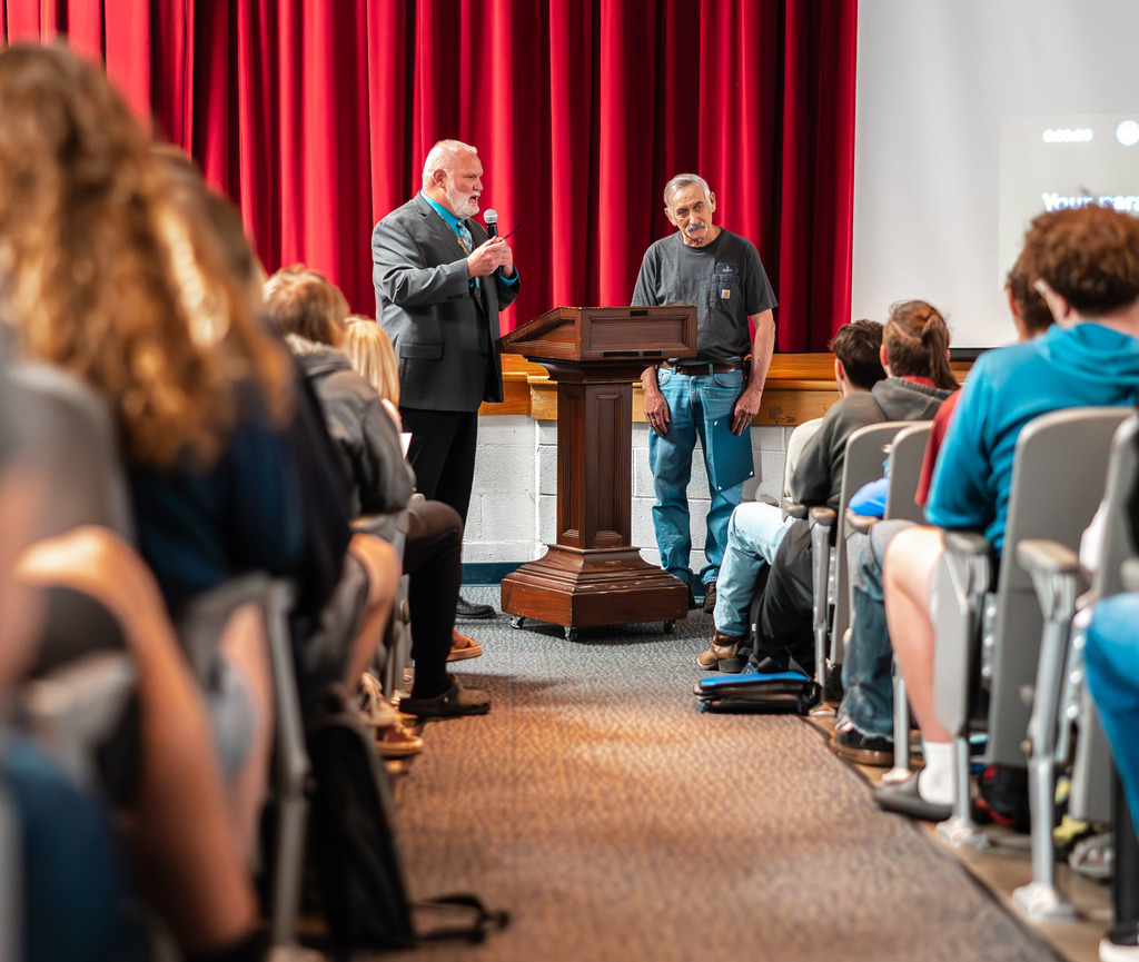 Kenneth Lacy standing at the front of the school's auditorium while the SAHS VP, Tank, reads a short bio of Kenneth.