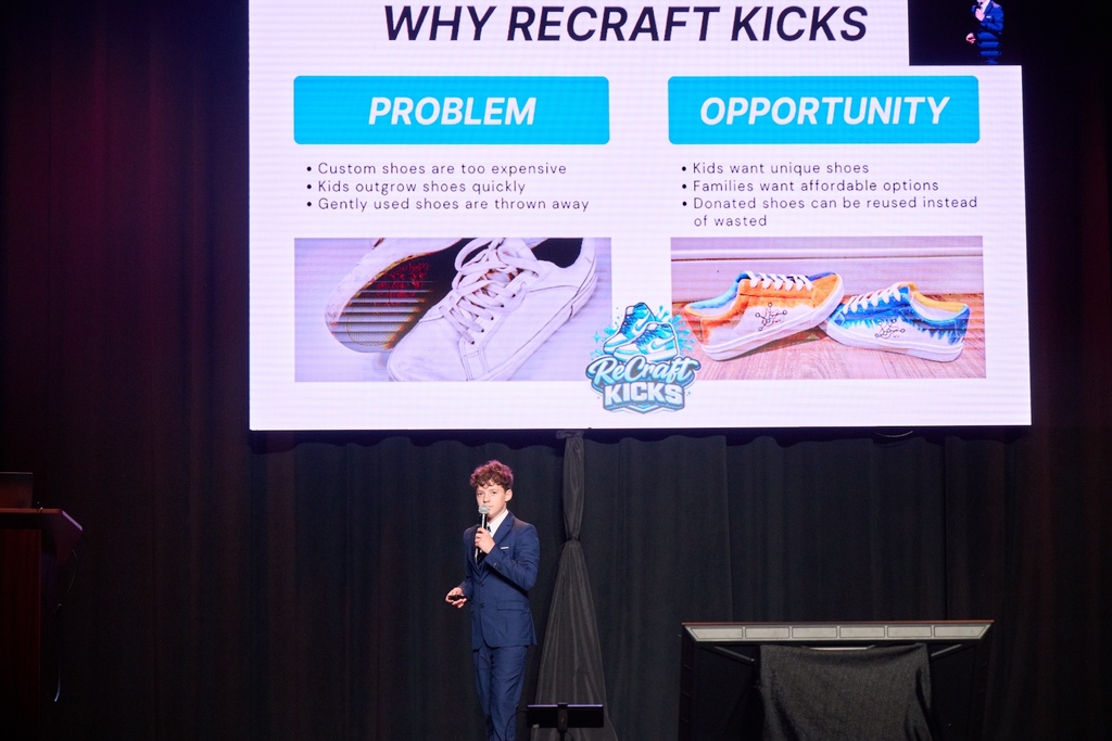 Parker is presenting on stage during the competition. He is holding a microphone. Behind him, his presentation is on a large screen. The slide that is showing says  Problem and Opportunity. 