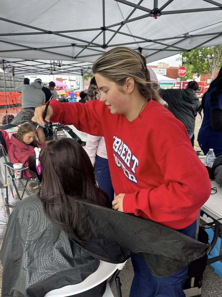 A Carver Beauty Academy student is separating a woman's hair for her haircut.. The woman receiving the haircut who is seated and wearing a black barber cape.