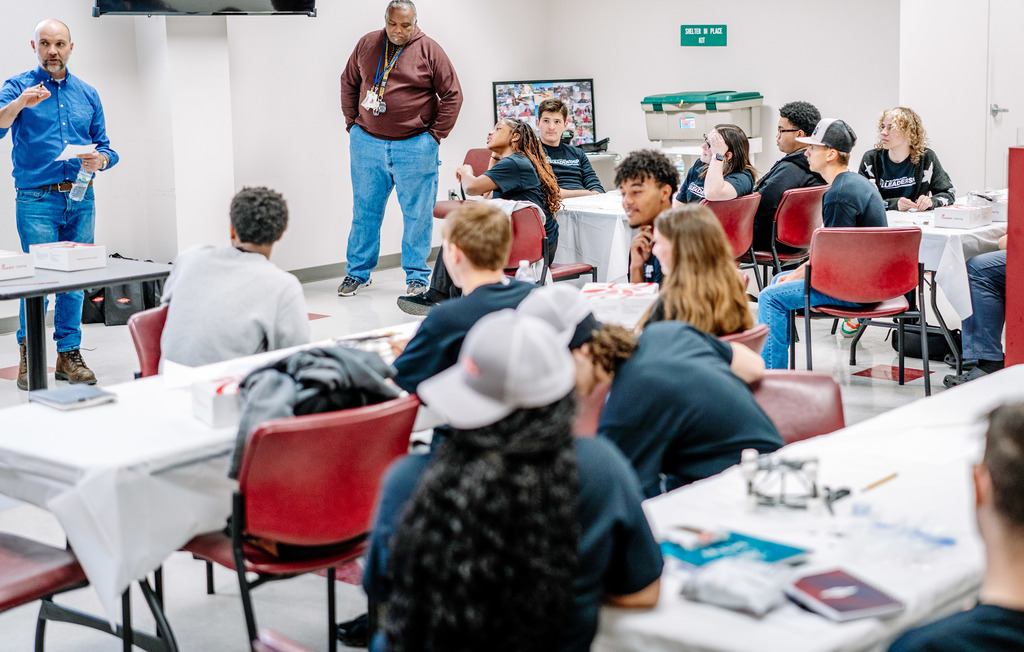 A classroom at Dow. Students are sitting at groups at different tables as Dow employees talk to them. 