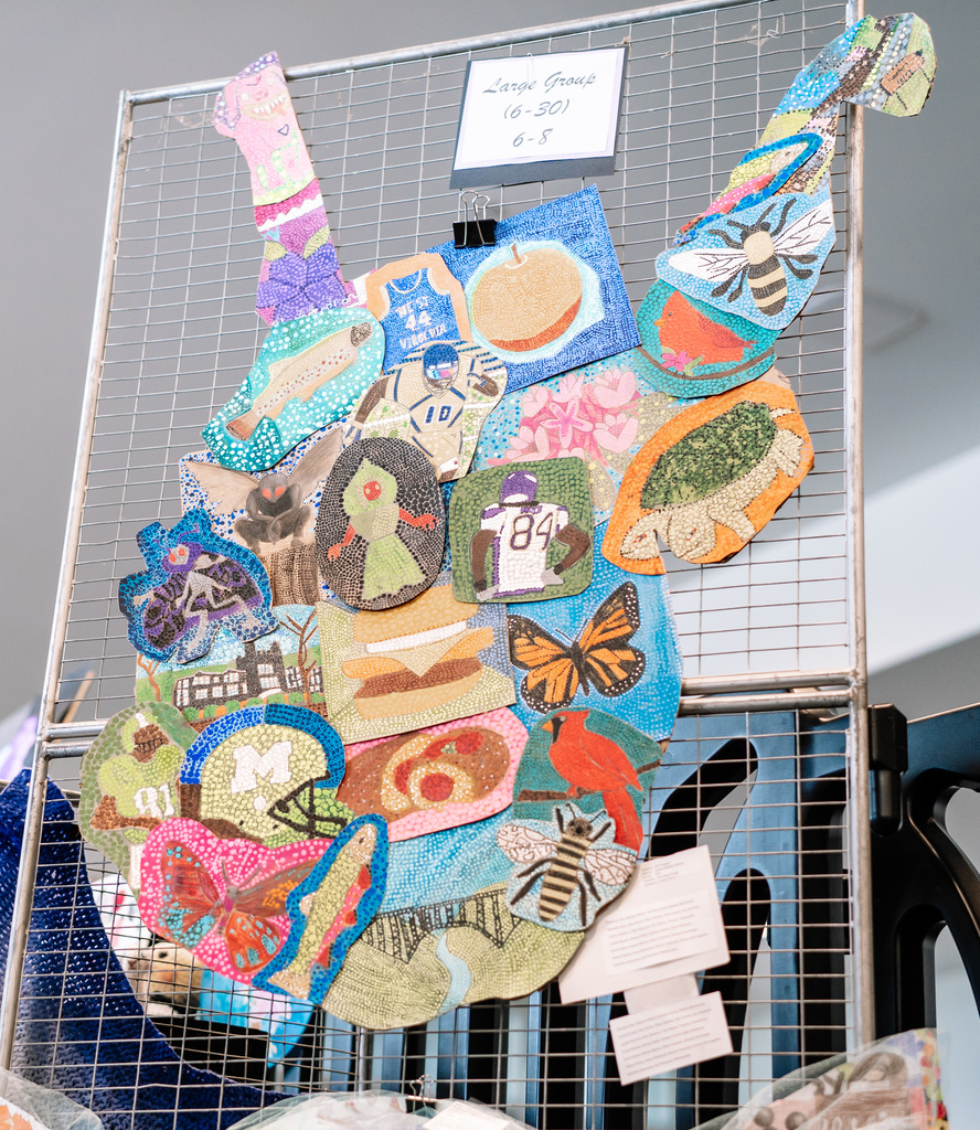 A large cutout of the state of West Virginia, with different West Virginia icons painted on smaller pieces of paper. Randy Moss in a Vikings uniform, the mothman, Steve Slaton, a Cardinal are just a few of the WV icons featured on this piece.