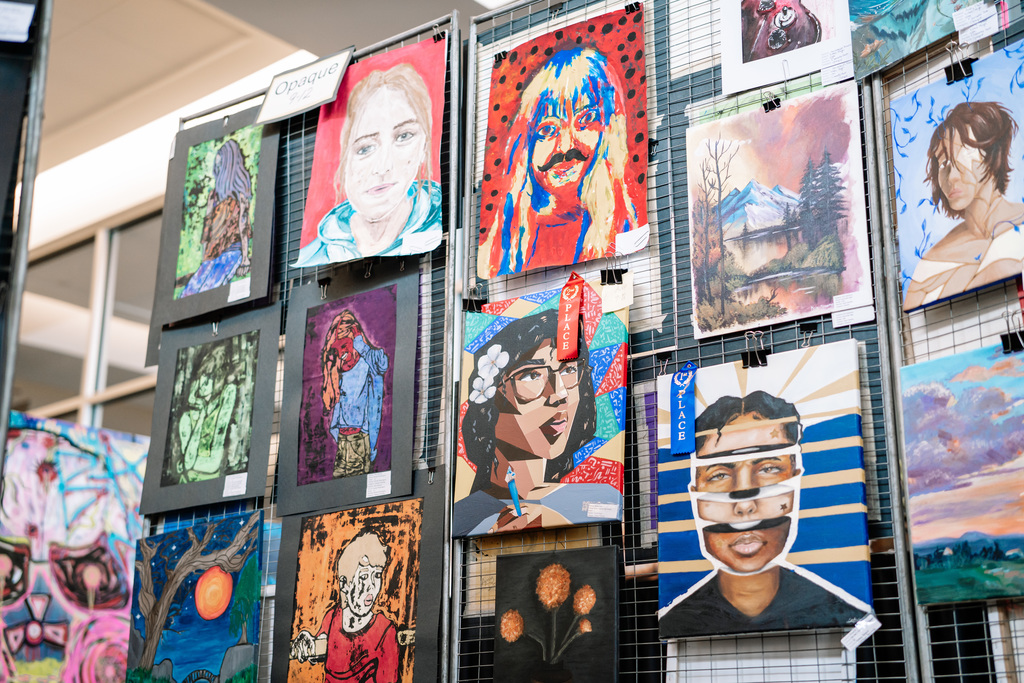 Several different pieces of art hanging on a wire frame at the KCS Art Show.