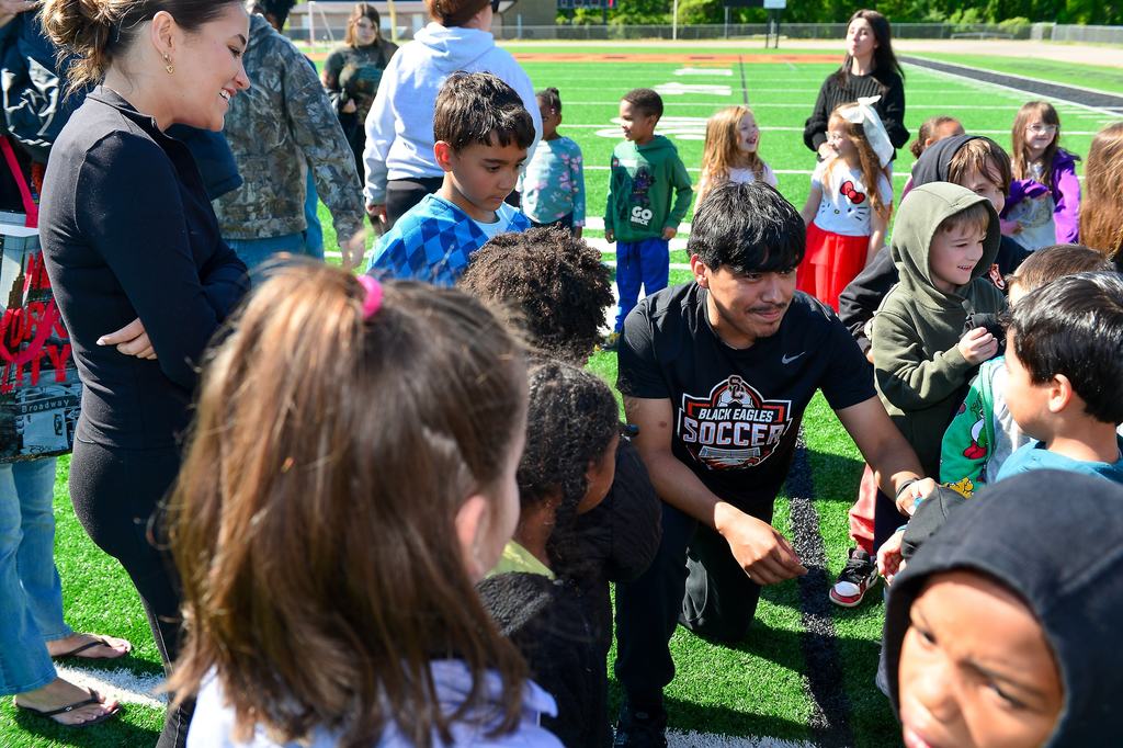 A high school student is down on one knee giving a fist bump to a young elementary student.