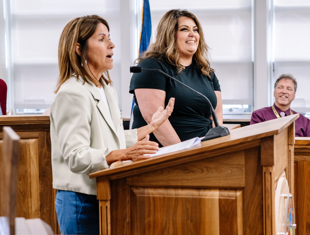 2026 KCS Teacher of the Year, Stephanie Elkins, is laughing in response to something Dr. Potter said while recognizing Stephanie. Dr. Potter is standing to Stephanie's right and is speaking into a mic on the podium.