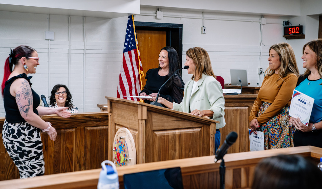 A teacher is laughing while walking up to receive her award. Dr. Potter is standing behind a podium and holding out the certificate and smiling. Beside Dr. Potter, Asst. Superintendent of Elementary Amanda Mays is laughing as well. 