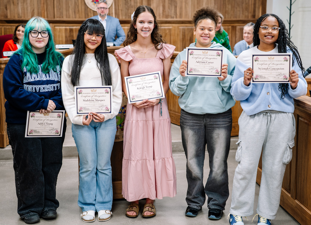 Five eighth grade students standing in front of the kcs board room holding their certificates for earning the 2026 Golden Horseshoe award.