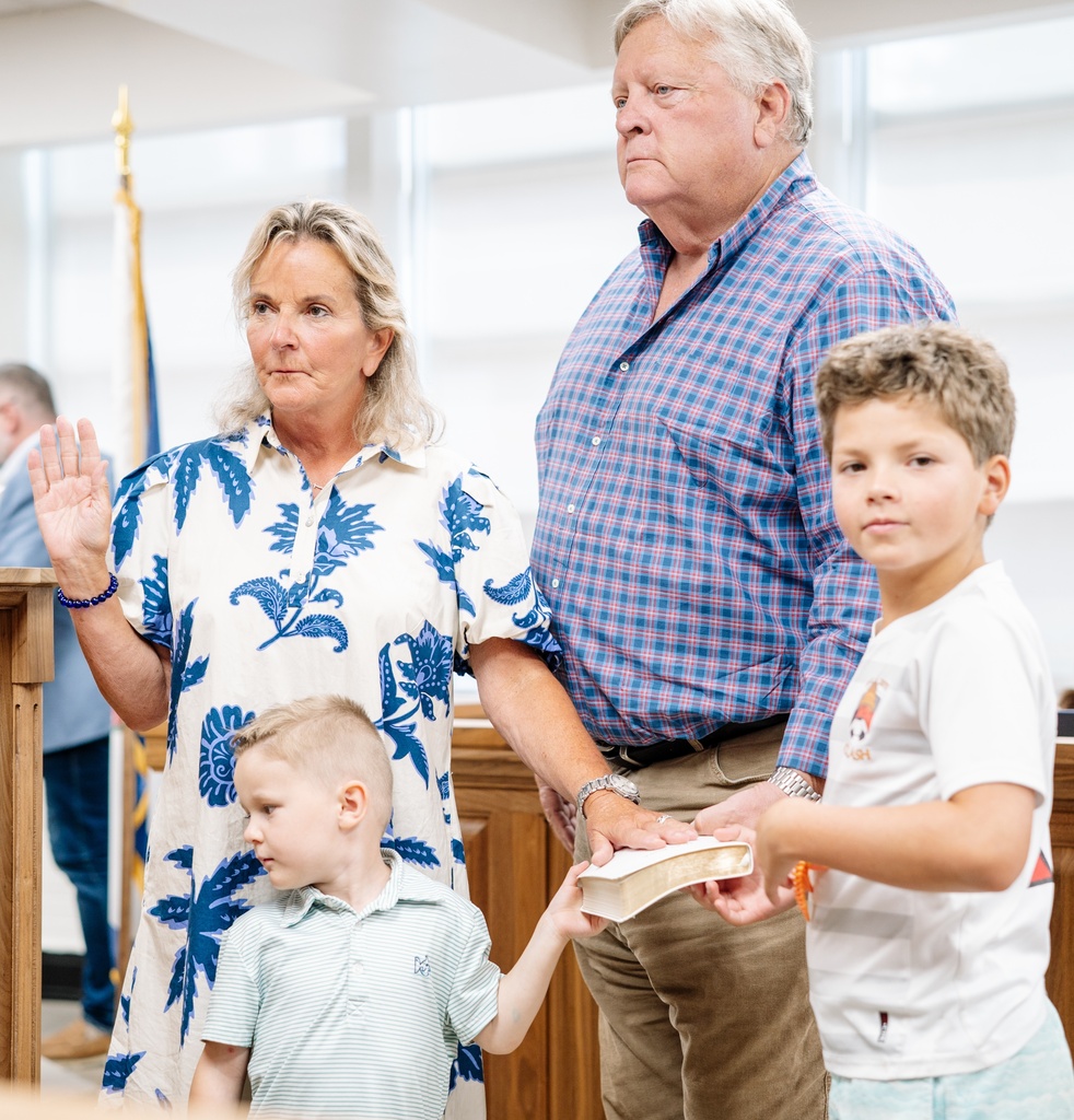 KCSBOE member Becky Jordan taking the oath of office. Her right hand is raised and her left hand is on a Bible that is being held by her husband and two young grandchildren.