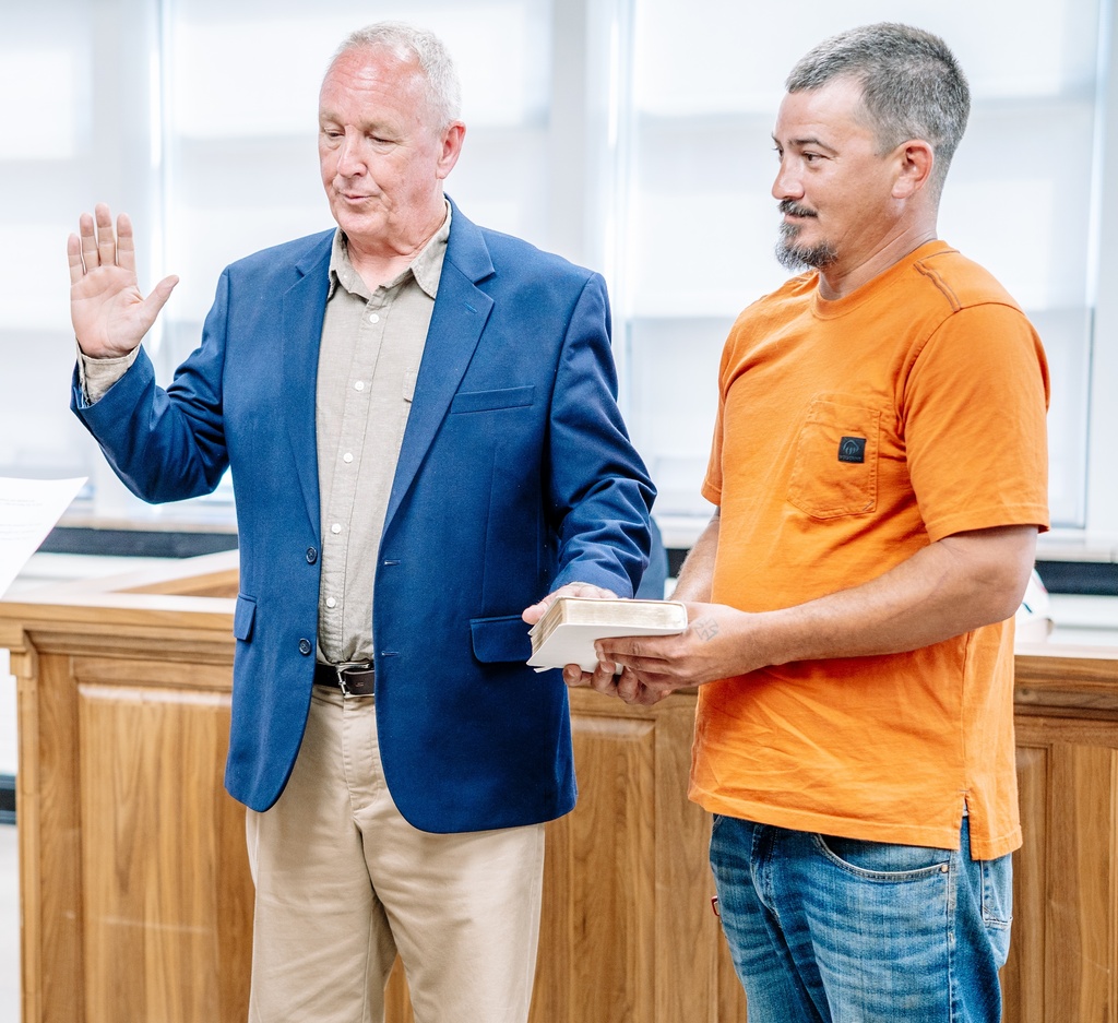 KCSBOE Member Mike Arbogast taking the oath of office. His right hand is raised and his left hand is on a Bible that is being held by his adult son.