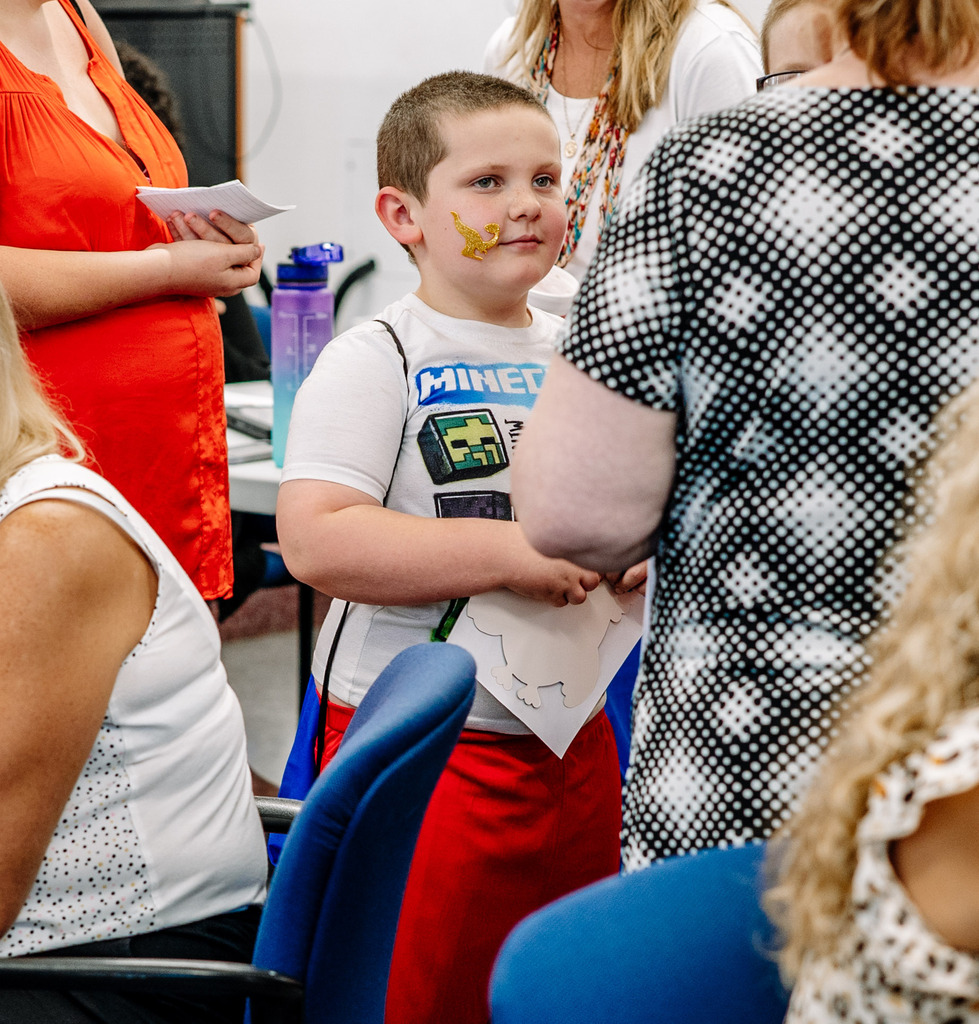 A young student with a gold dinosaur sticker on his cheek. 