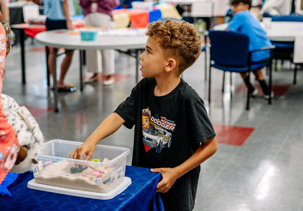 A young student looking off to his right while playing with small toys in a sensory box. 