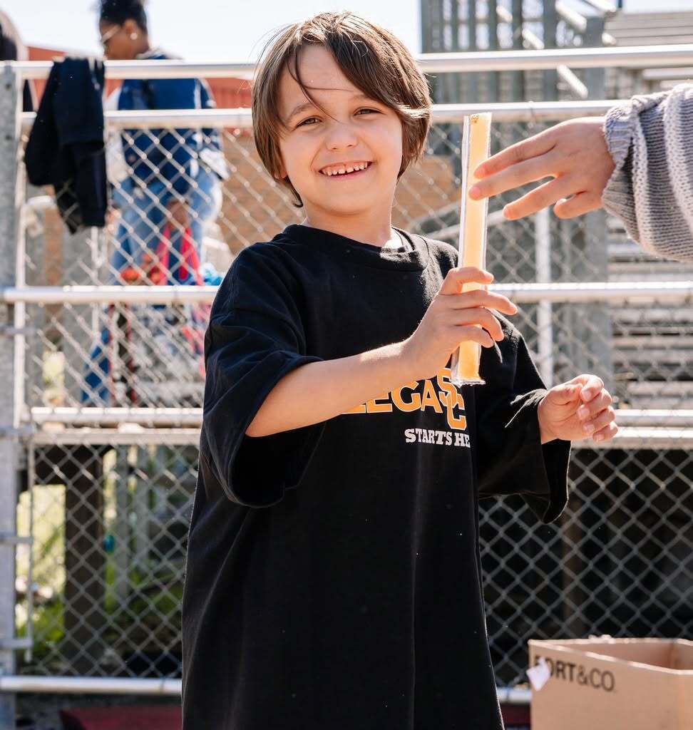 young student smiling at the camera reaching for a popsicle.