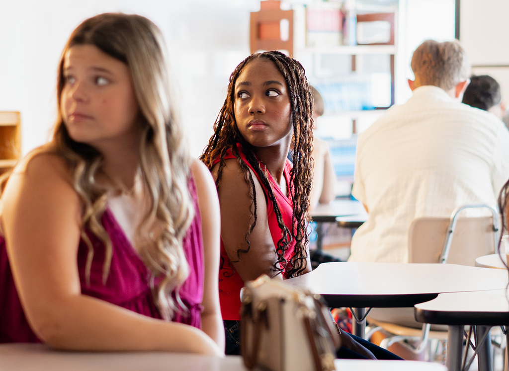 Two students sitting at a tabler in their classroom and looking back toward their teacher who is not pictured.