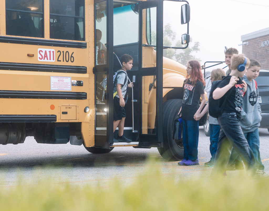 A student stepping off a school bus while others are waiting to board the bus. 