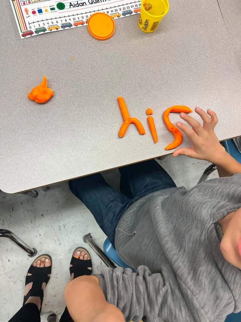 The word Hi, on top of a student's desk, spelled out in orange play-doh.