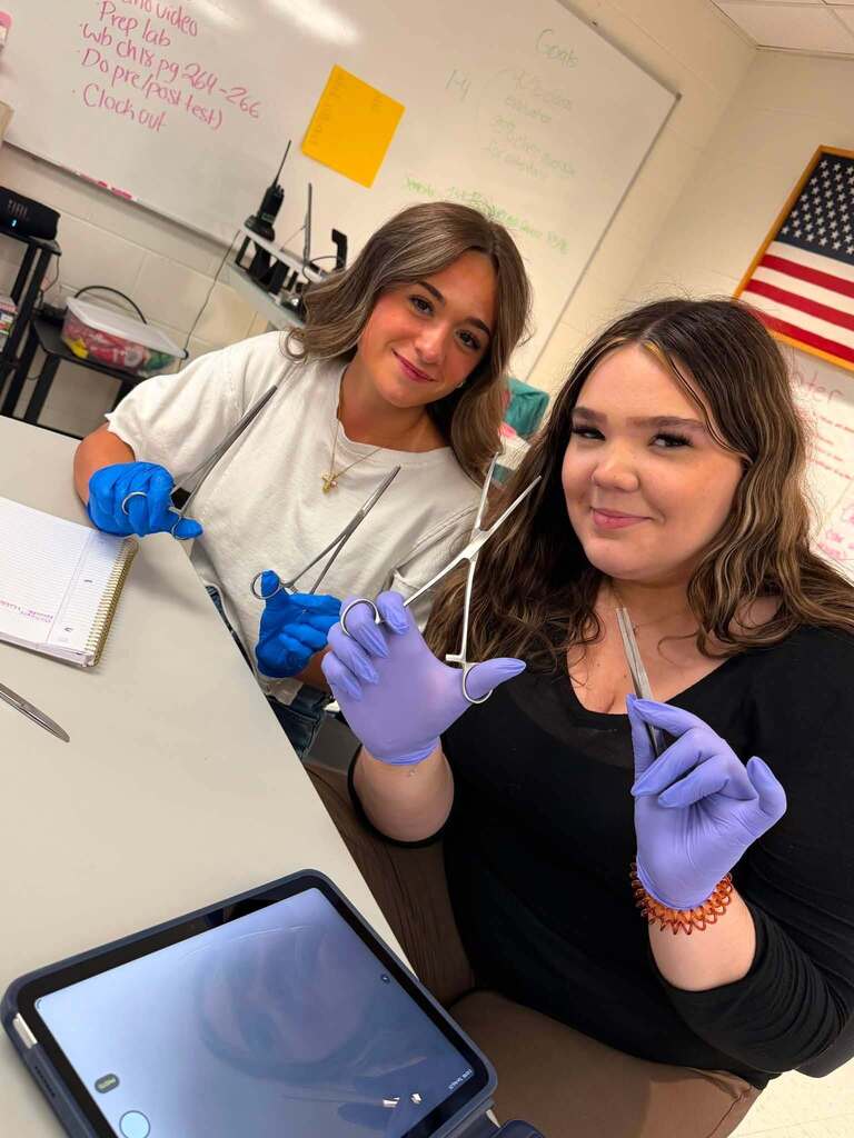 Two medical assistant students are posing for a picture with their clamps and tweezers for their medical lab.