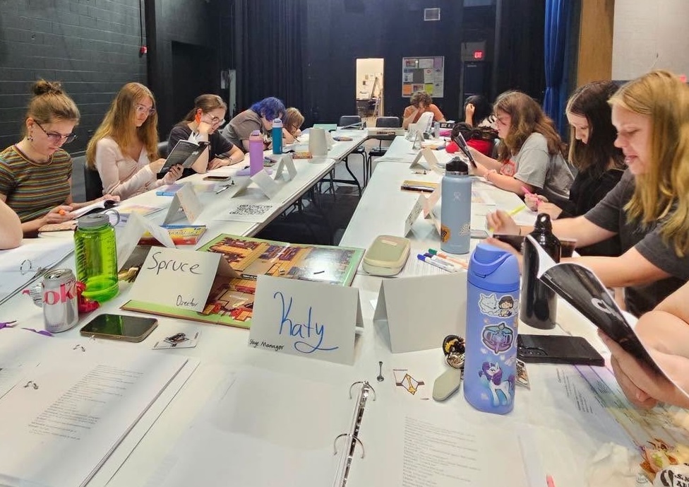 Students sitting around a table doing a read through of a play their school is putting on later this fall.
