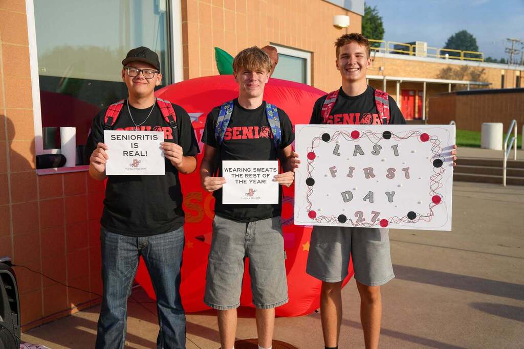 three high school seniors holding signs about this being their last first day of school on the first day of school.