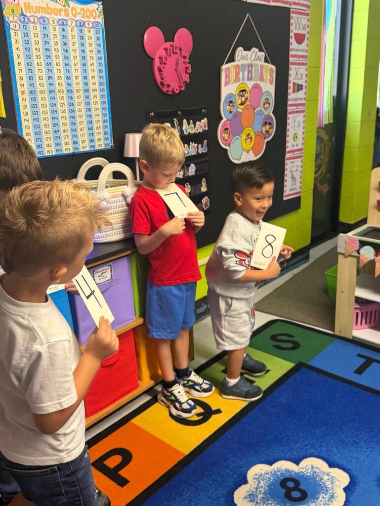One student is holding a small white board that has the number seven written on it and another is holding a similar board but it has the number 8 on it.