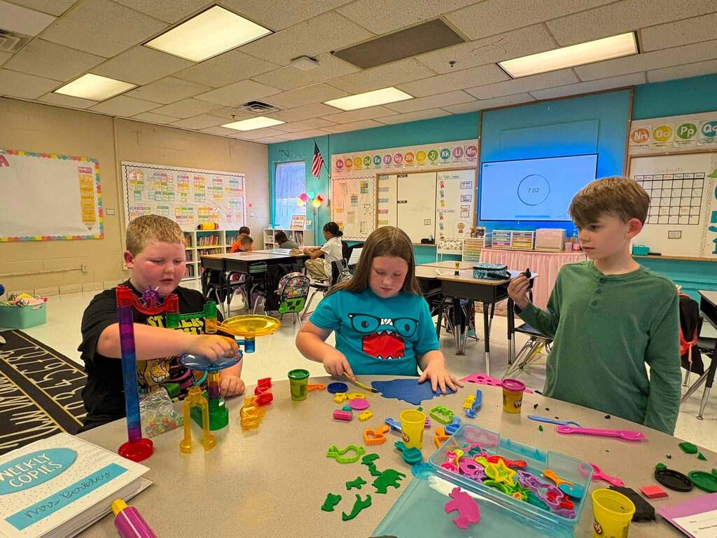 Three students sitting at a classroom table building towers out of plastic tubing and making shapes with play-doh.