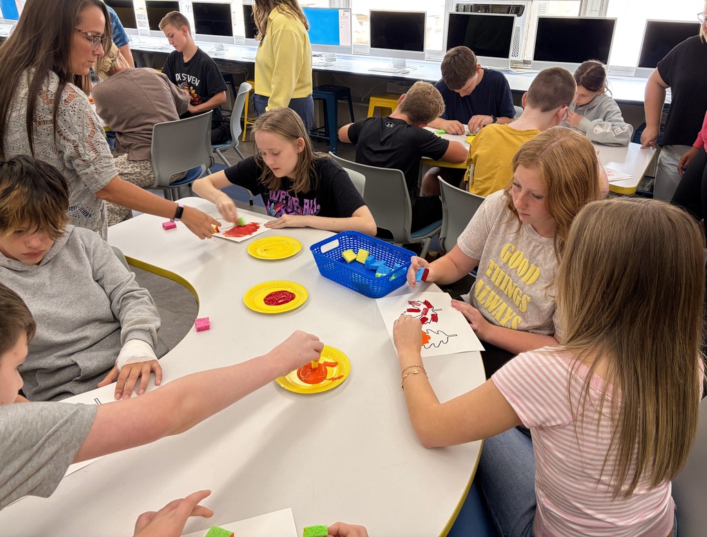 Students sitting together at a classroom table and painting.