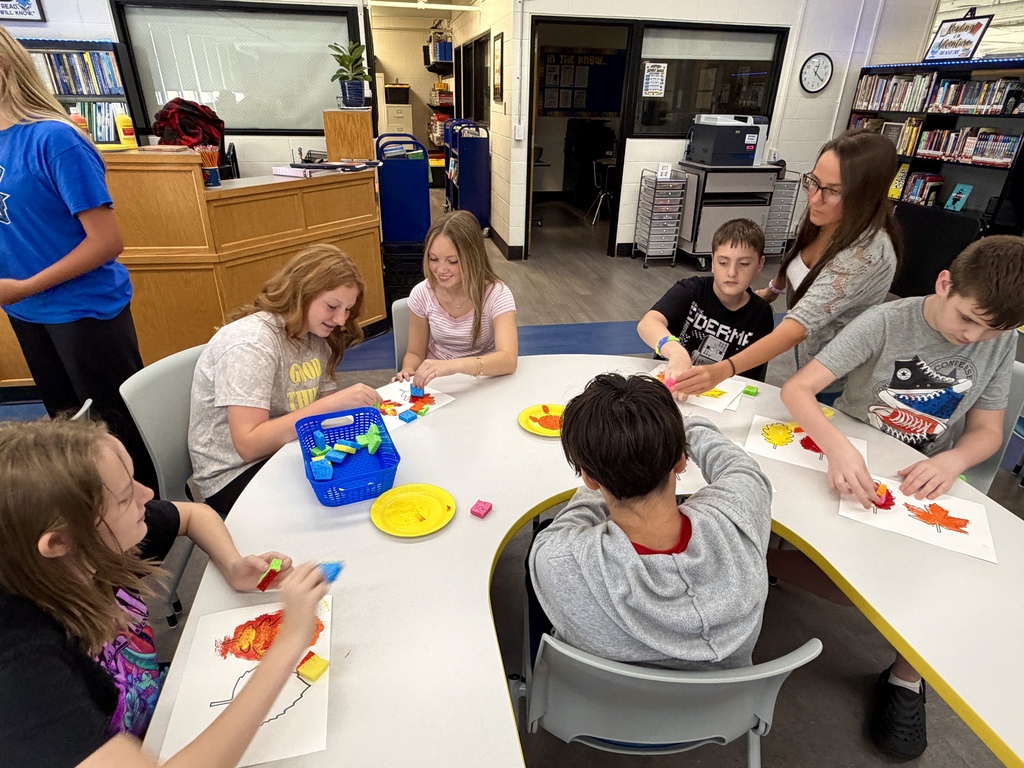 Students sitting together at a classroom table and painting leaves.