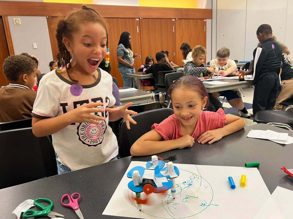 Two students excited about a robot they created out of markers. 