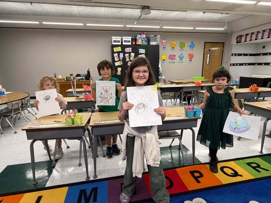 students holding a picture of a spider in a web that they drew.