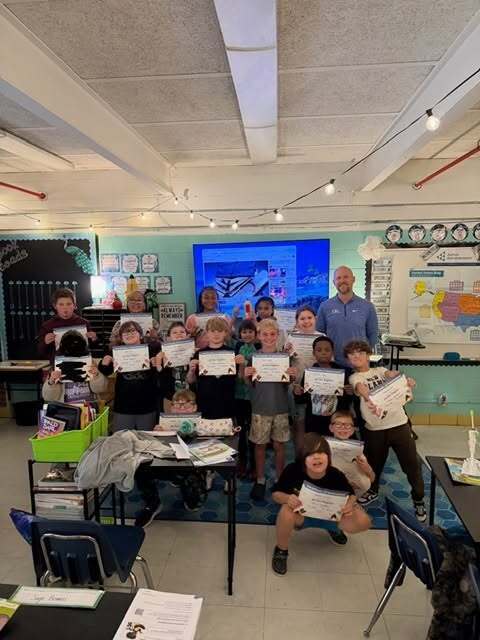A group of students is posing for a picture with their certificates of completion with the adult volunteer who came in to teach them about his job. 