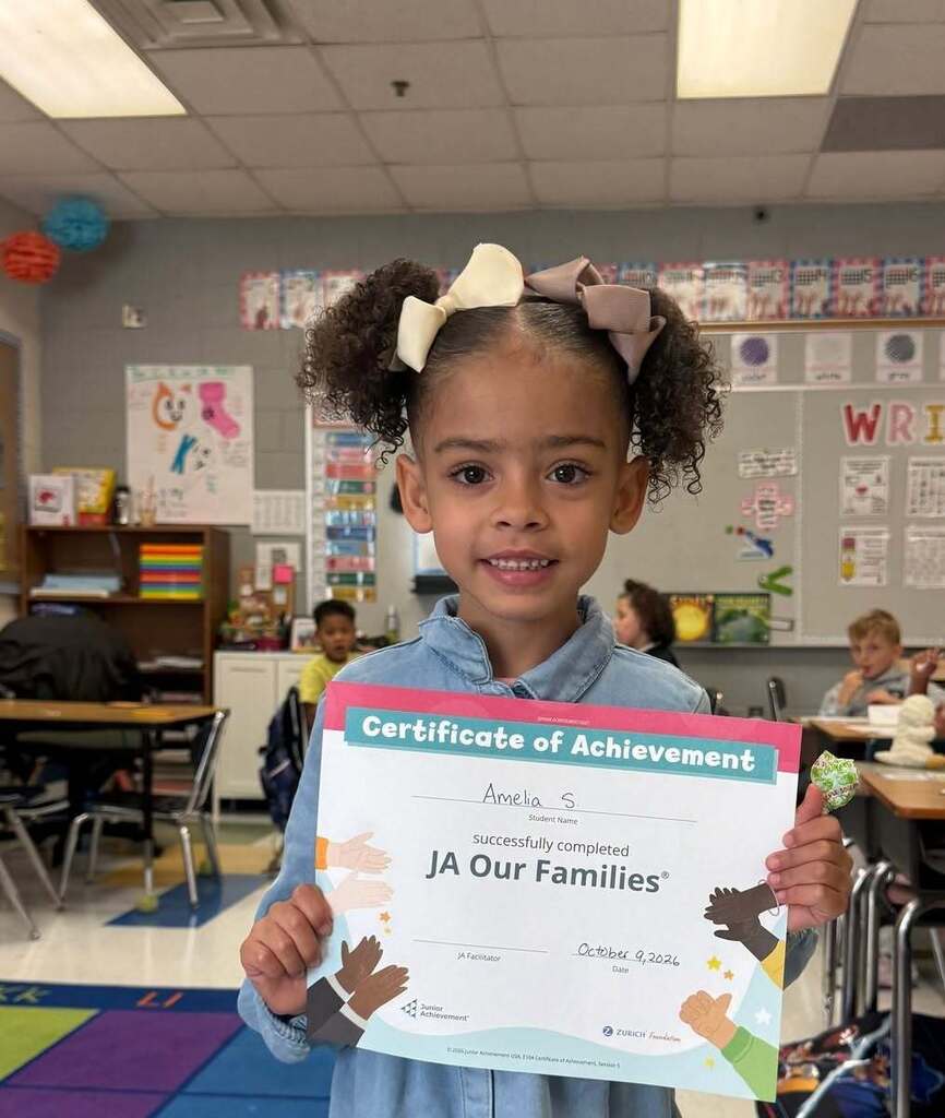 A student is proudly holding up her "Certificate of Achievement" for completing the Junior Academy "Our Families" lesson. 