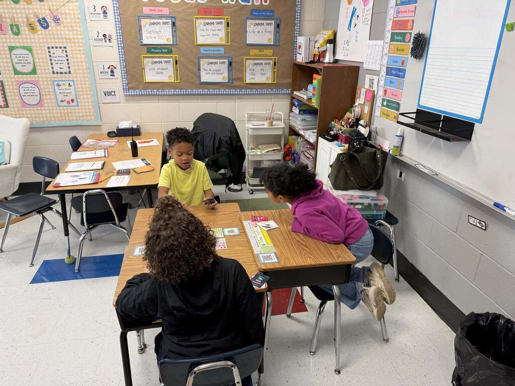 Three students sitting at their desks and working on an assignment together. The students desk are pushed together in the shape of a T.