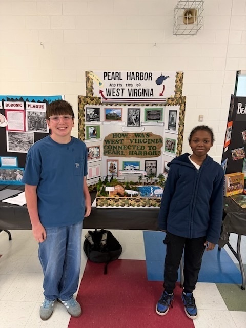 two students standing in front of their social studies fair presentation about Pearl Harbor and its ties to West Virginia.
