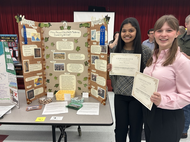 two students standing beside their social studies fair project which is titled,  "How Ancient Architects Mastered Durability We Lost."