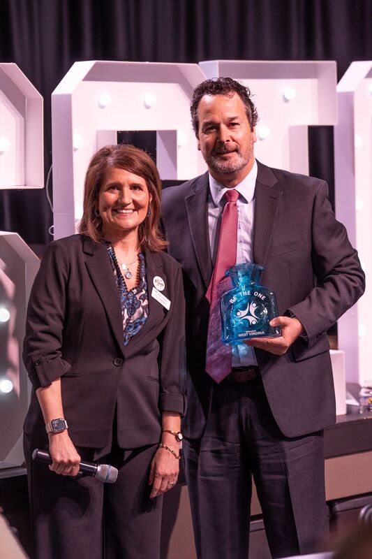 Jon Duffy holding his award, a blue Blinko Glass vase, and posing for a picture with Mission WV Executive Director Kelley Thompson. 